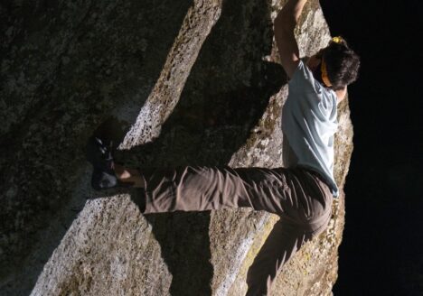 young man climbing a sheer rock face, reaching up with one hand