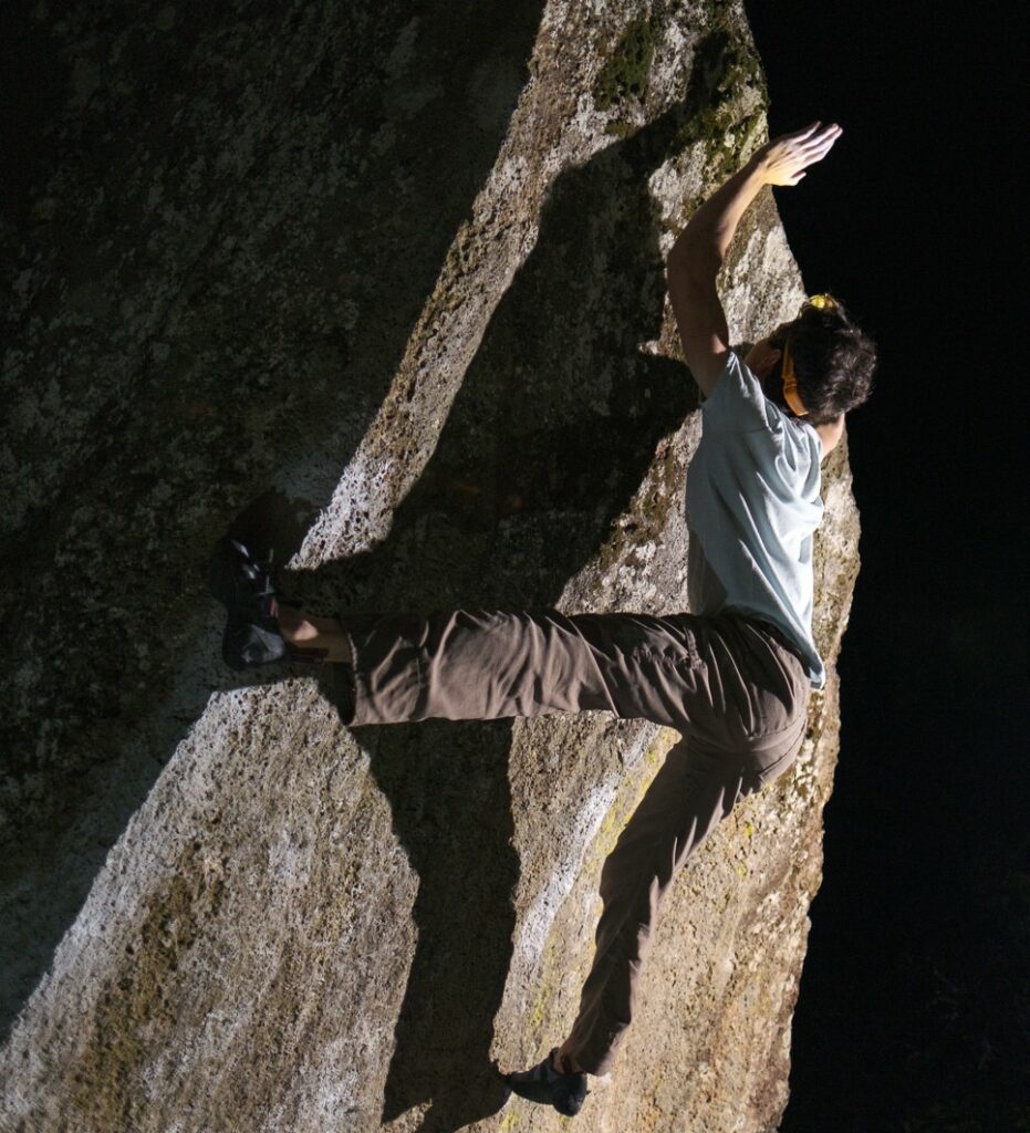 young man climbing a sheer rock face, reaching up with one hand